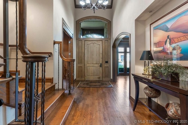 foyer entrance featuring an inviting chandelier, a towering ceiling, stairway, arched walkways, and dark wood finished floors