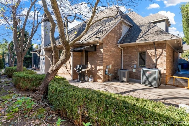 back of house featuring roof with shingles, a patio, central AC, and brick siding