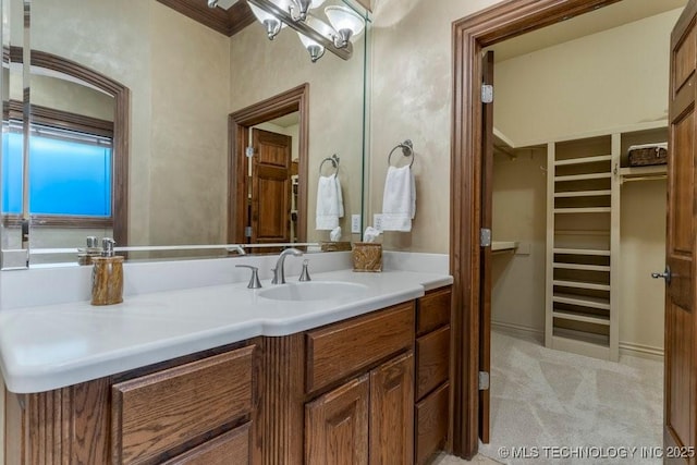 bathroom with an inviting chandelier, ornamental molding, a walk in closet, and vanity