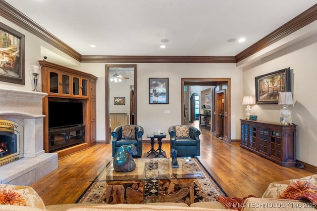 living room featuring crown molding, a ceiling fan, a lit fireplace, and wood finished floors