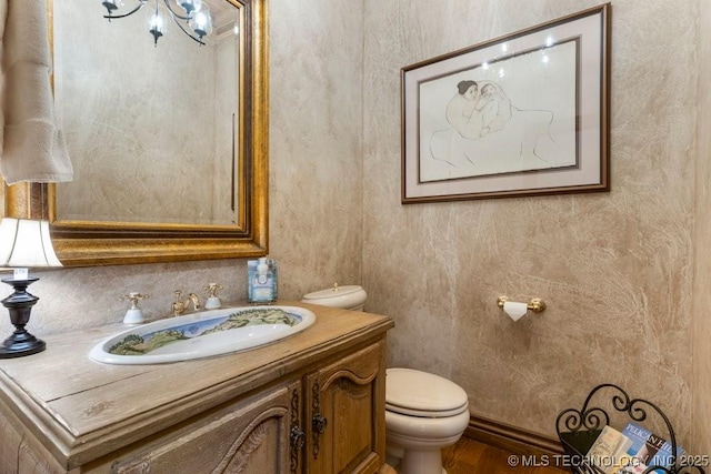 half bath featuring vanity, toilet, wood finished floors, and a notable chandelier