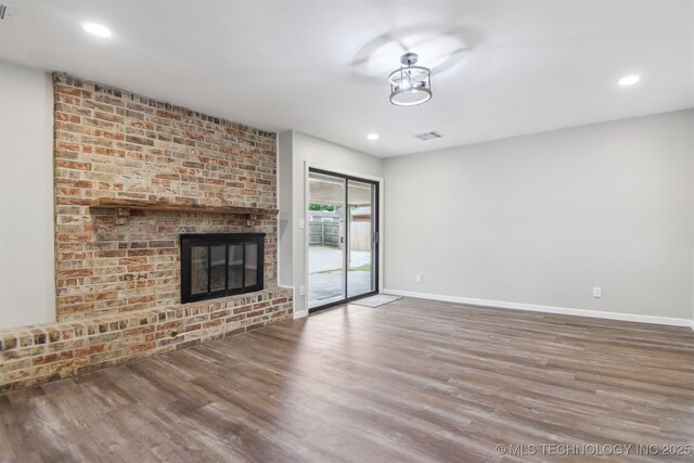 unfurnished living room with a brick fireplace, recessed lighting, baseboards, wood finished floors, and visible vents