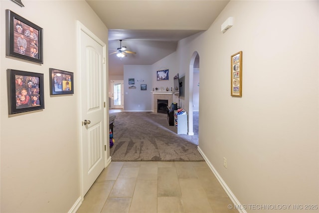 corridor with lofted ceiling, light tile patterned flooring, baseboards, light colored carpet, and arched walkways