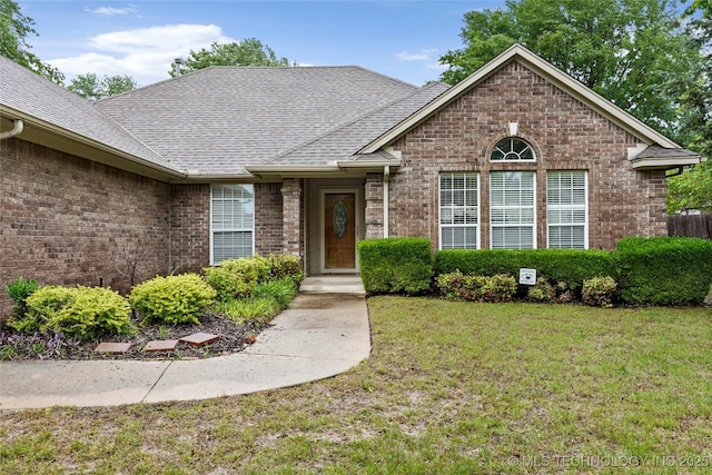 view of front of home with roof with shingles, a front yard, and brick siding