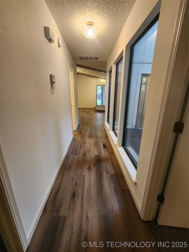 hall featuring visible vents, a textured wall, baseboards, a textured ceiling, and dark wood finished floors