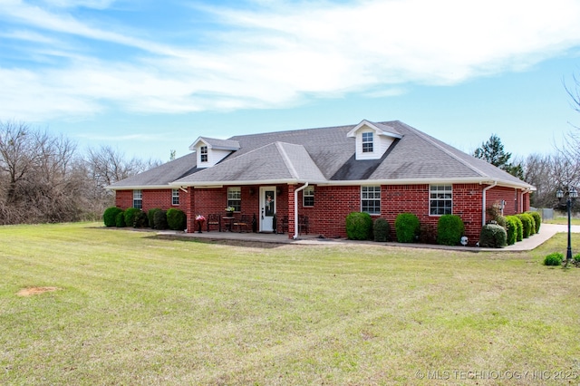 new england style home with brick siding, a shingled roof, a patio area, and a front lawn