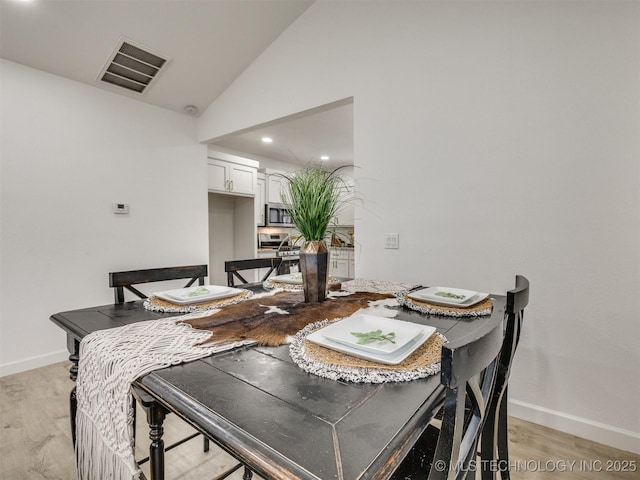 dining space featuring visible vents, light wood finished floors, baseboards, and high vaulted ceiling