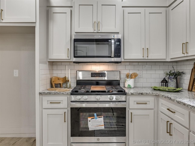 kitchen with white cabinets, light stone counters, stainless steel appliances, wood finished floors, and tasteful backsplash