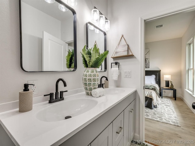 ensuite bathroom with double vanity, a sink, connected bathroom, and wood finished floors