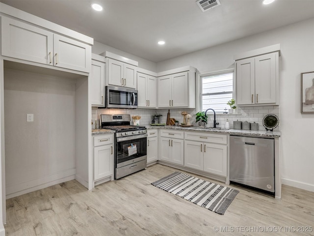 kitchen with visible vents, baseboards, a sink, light wood finished floors, and appliances with stainless steel finishes
