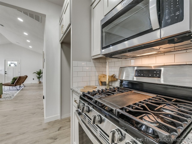 kitchen featuring decorative backsplash, vaulted ceiling, baseboards, light wood finished floors, and stainless steel appliances