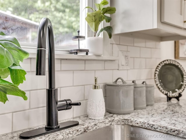 interior details with a sink, white cabinetry, light stone countertops, and tasteful backsplash