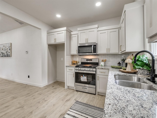 kitchen featuring light stone counters, tasteful backsplash, a sink, stainless steel appliances, and light wood-type flooring