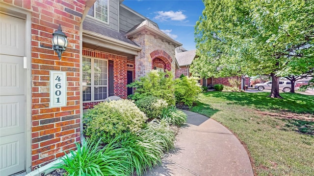 doorway to property with brick siding, roof with shingles, and a lawn