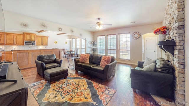 living area with arched walkways, a ceiling fan, vaulted ceiling, and wood finished floors