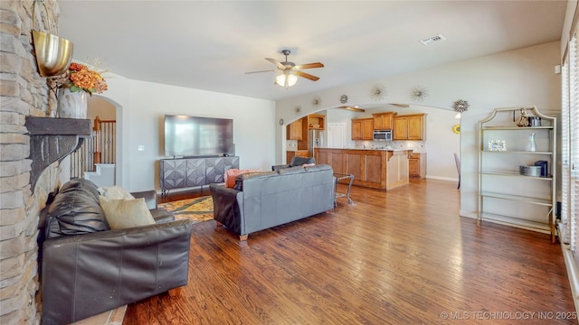 living room featuring arched walkways, ceiling fan, visible vents, and wood finished floors