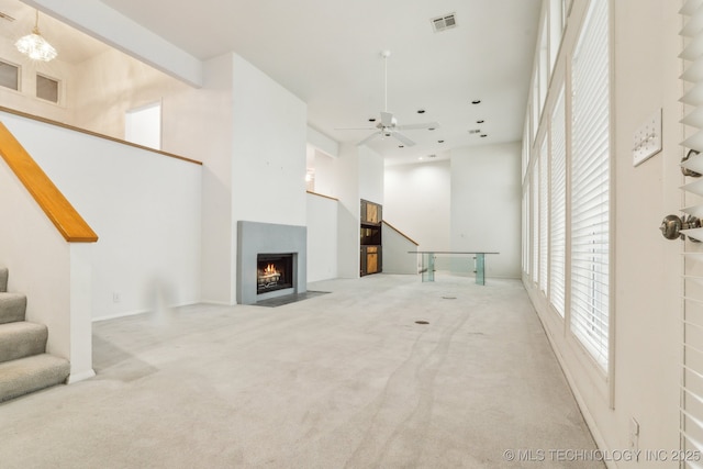 unfurnished living room featuring a fireplace with flush hearth, stairs, a towering ceiling, and ceiling fan