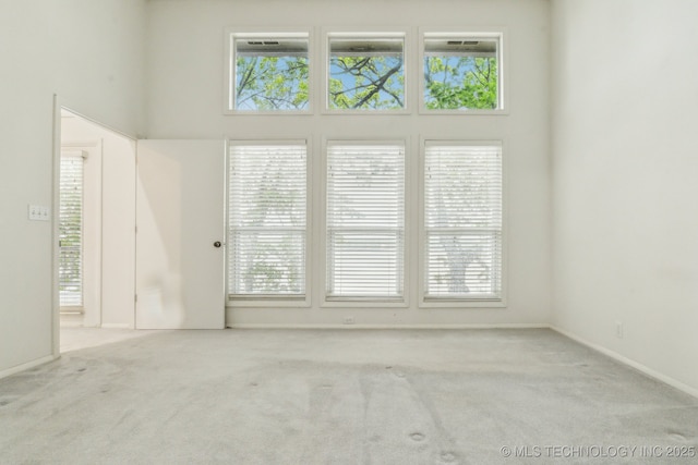 carpeted spare room with a towering ceiling, baseboards, and a wealth of natural light