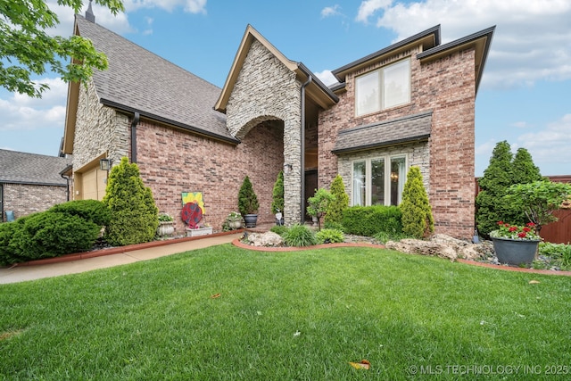 view of front of house with stone siding, a front yard, roof with shingles, brick siding, and an attached garage