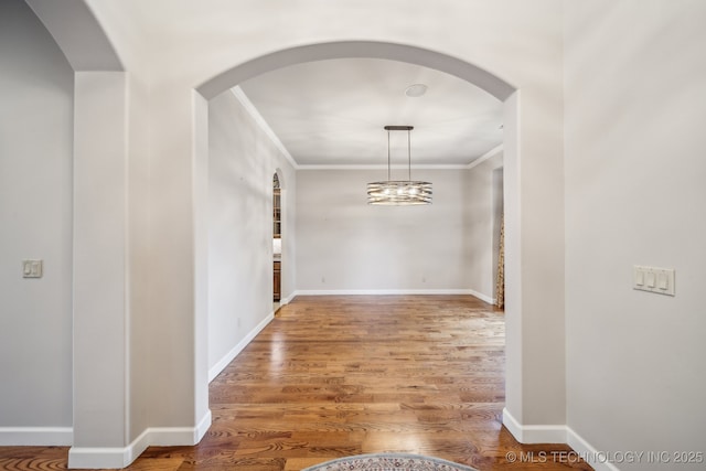 interior space with baseboards, ornamental molding, arched walkways, and wood finished floors