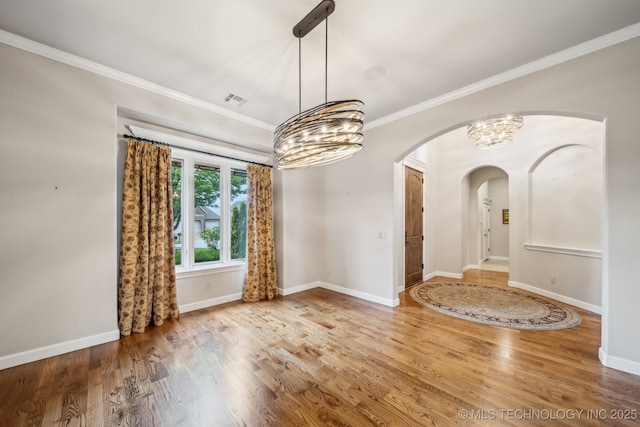 unfurnished dining area with an inviting chandelier, crown molding, wood finished floors, baseboards, and arched walkways
