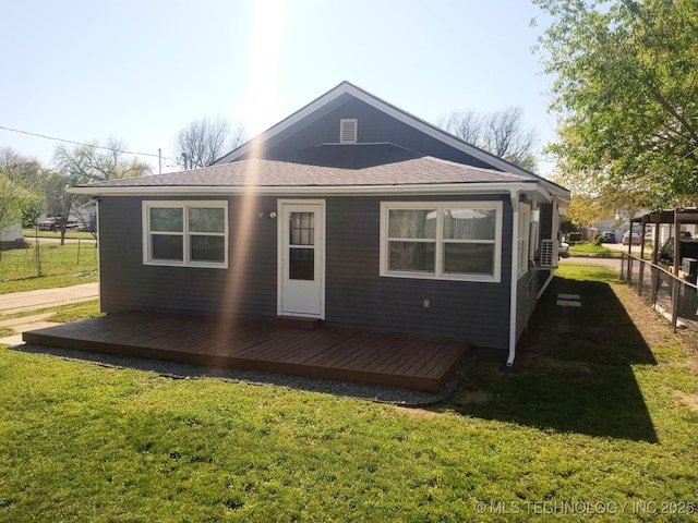 back of house featuring a yard, a deck, fence, and a shingled roof