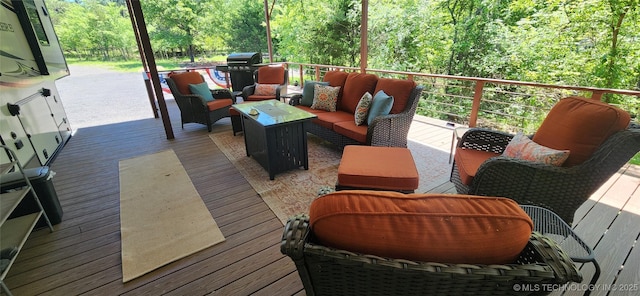 wooden deck featuring a view of trees, an outdoor hangout area, and a grill