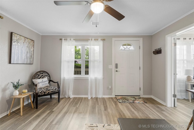 entrance foyer featuring light wood-style floors, a ceiling fan, baseboards, visible vents, and ornamental molding