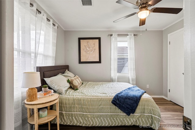 bedroom featuring ceiling fan, visible vents, crown molding, wood finished floors, and baseboards
