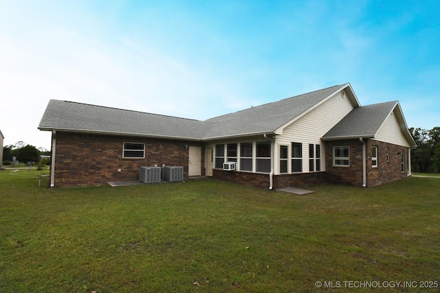 back of property with brick siding, central AC unit, a lawn, and a sunroom
