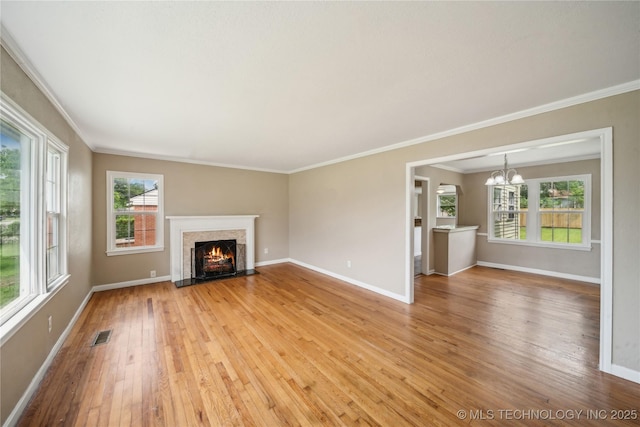 unfurnished living room featuring crown molding, baseboards, light wood finished floors, and a chandelier