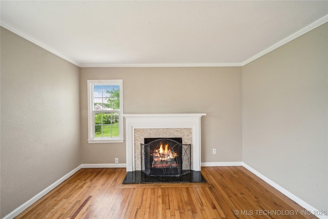 unfurnished living room with baseboards, ornamental molding, wood finished floors, and a warm lit fireplace