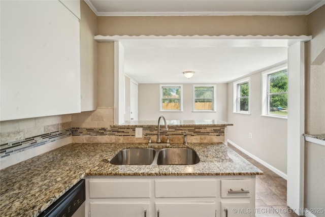 kitchen with a peninsula, white cabinetry, tasteful backsplash, a sink, and stone counters