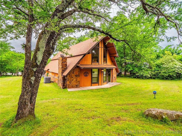 back of property with a lawn, central AC unit, stone siding, and a shingled roof