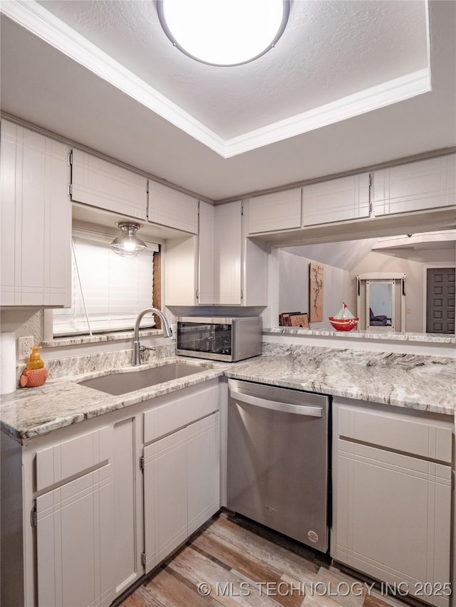 kitchen featuring a sink, a raised ceiling, stainless steel appliances, white cabinetry, and light wood-type flooring