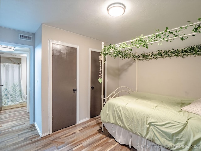 bedroom with two closets, baseboards, visible vents, and light wood-style flooring