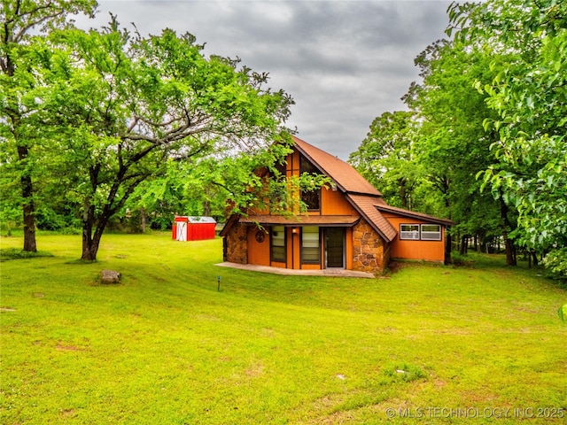 back of house with a storage unit, an outdoor structure, a yard, and stone siding