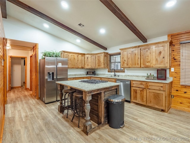kitchen with a sink, light wood-style floors, stainless steel appliances, vaulted ceiling with beams, and visible vents