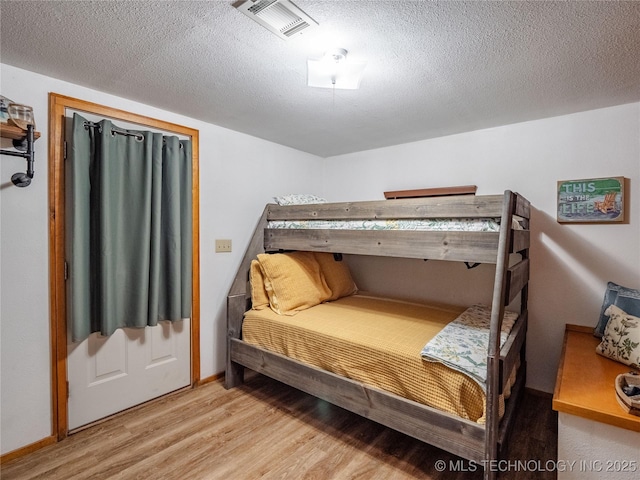bedroom with baseboards, light wood finished floors, a textured ceiling, and visible vents