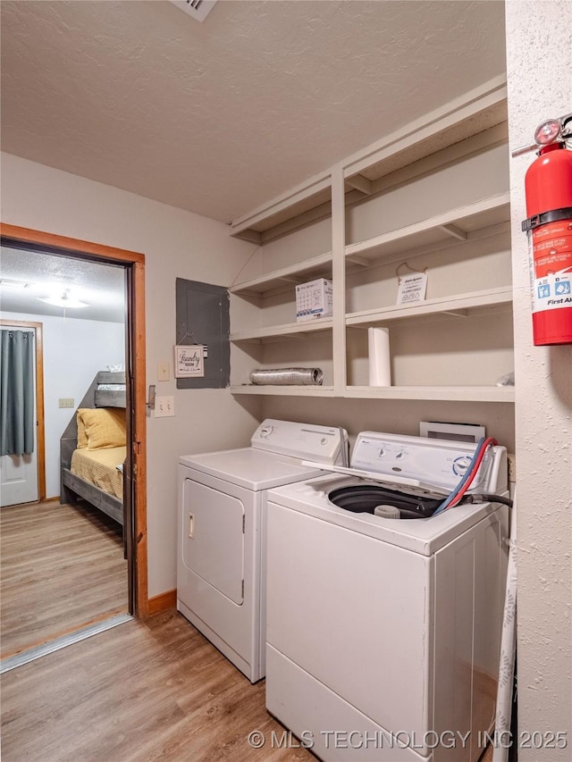 laundry area with laundry area, light wood-style floors, electric panel, and washer and dryer