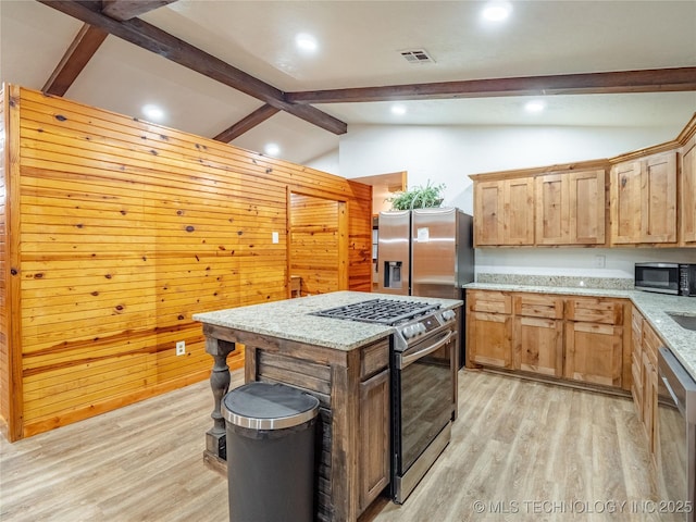 kitchen featuring appliances with stainless steel finishes, lofted ceiling with beams, light stone counters, light wood finished floors, and visible vents
