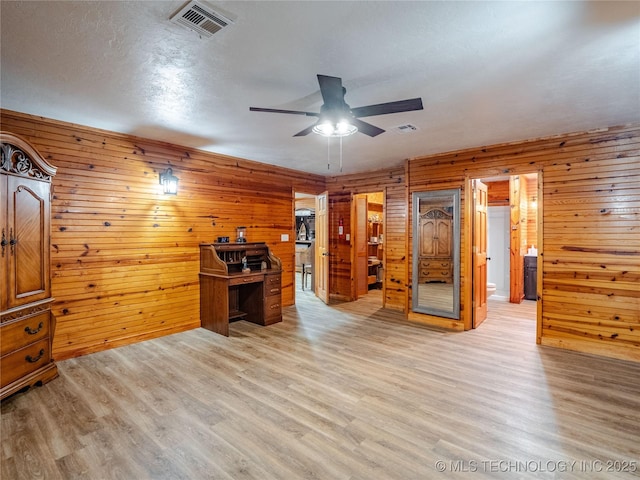 office area featuring wooden walls, a ceiling fan, visible vents, and light wood-style floors