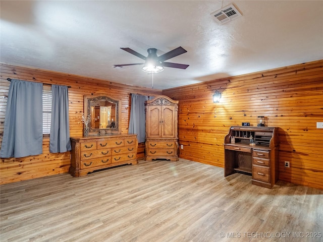 office area featuring wooden walls, ceiling fan, light wood-type flooring, and visible vents