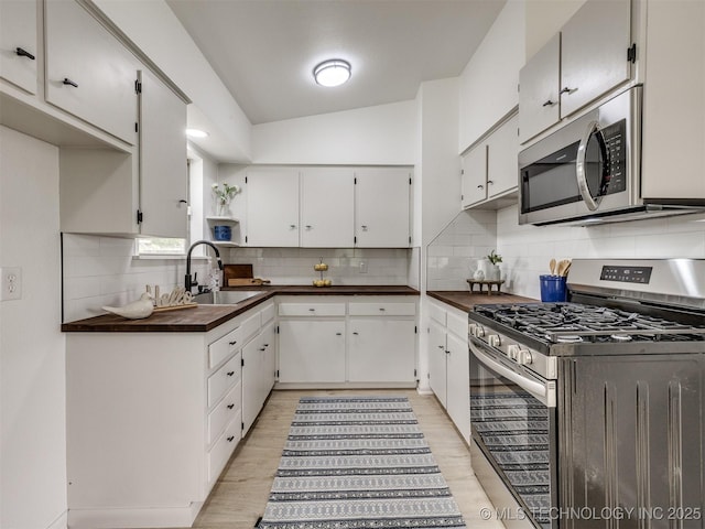 kitchen with dark countertops, appliances with stainless steel finishes, a sink, light wood-style floors, and decorative backsplash