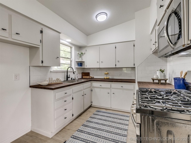 kitchen with open shelves, a sink, light wood-style flooring, backsplash, and stainless steel appliances