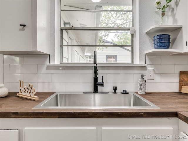 kitchen with backsplash, white cabinets, wooden counters, and a sink