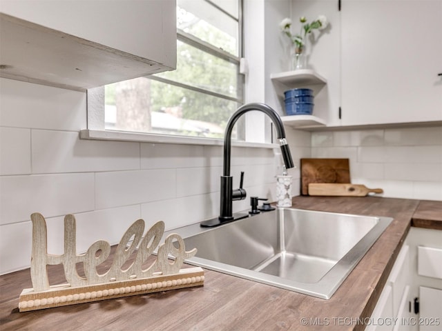room details featuring a sink, open shelves, white cabinets, and tasteful backsplash