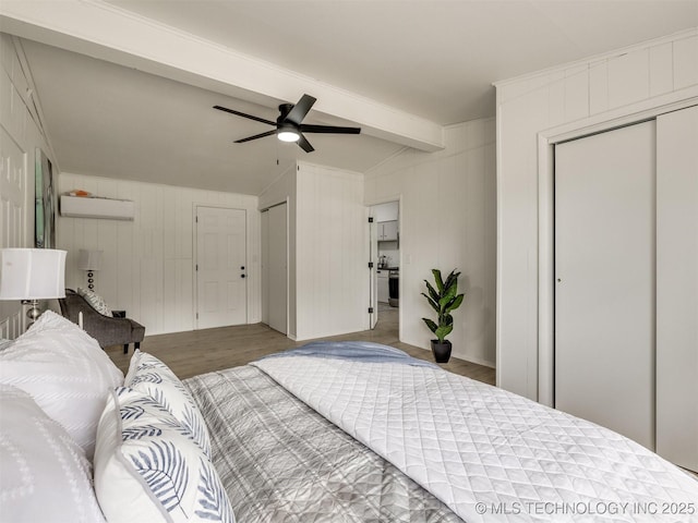 bedroom with ceiling fan, a wall unit AC, wood finished floors, lofted ceiling with beams, and two closets