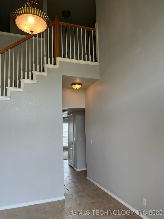 stairs featuring baseboards, tile patterned flooring, and a high ceiling