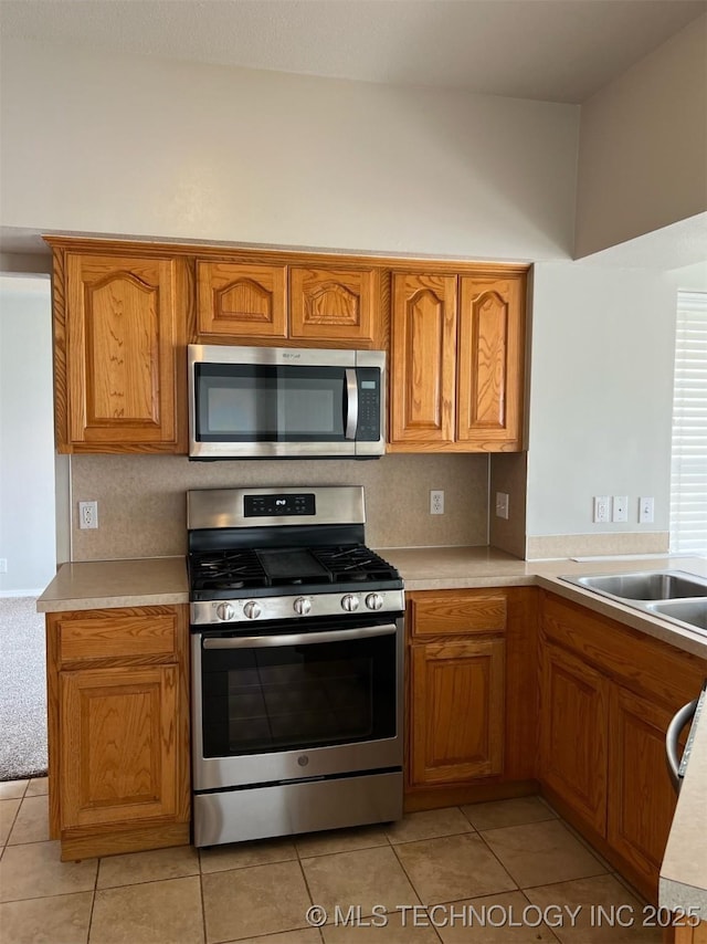 kitchen with brown cabinetry, light countertops, a sink, light tile patterned floors, and stainless steel appliances